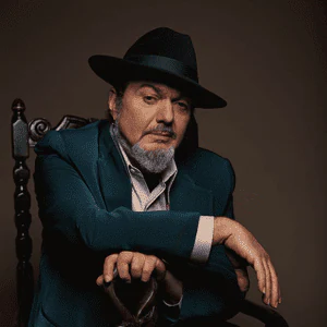 Dr. John seated in a teal suit and black hat.